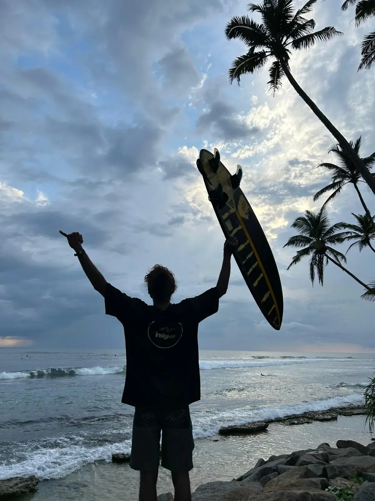 Surfer silhouetted against the sky, holding a board up by the sea