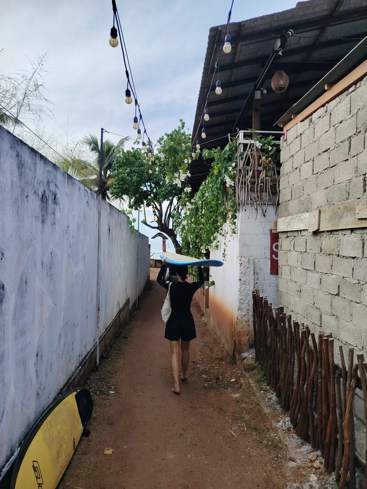 Surfer carrying a board down a narrow lane toward the beach