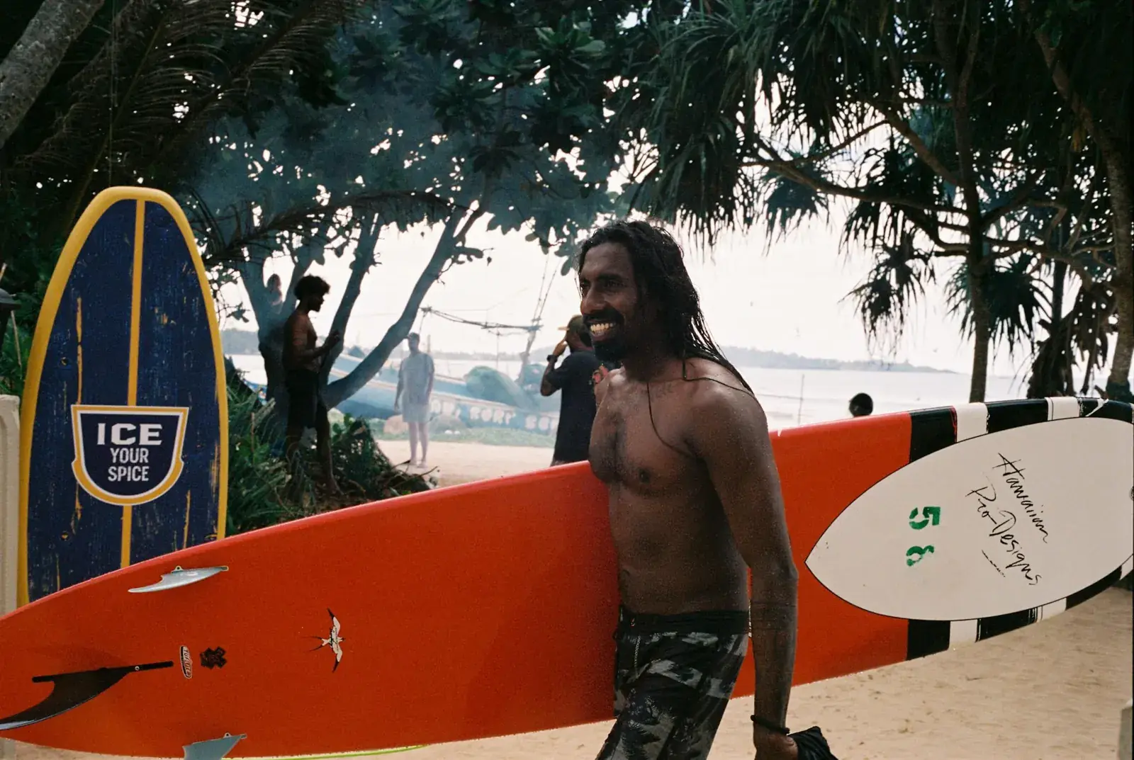 Instructor carrying an orange surfboard past a rack of boards