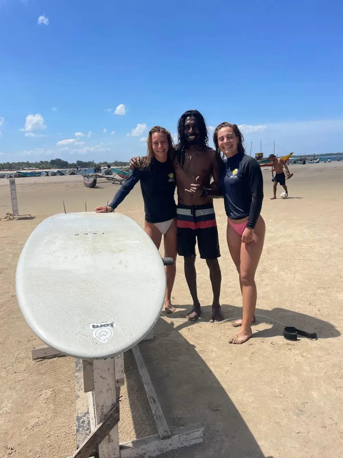 Instructor and two guests on the beach with a surfboard