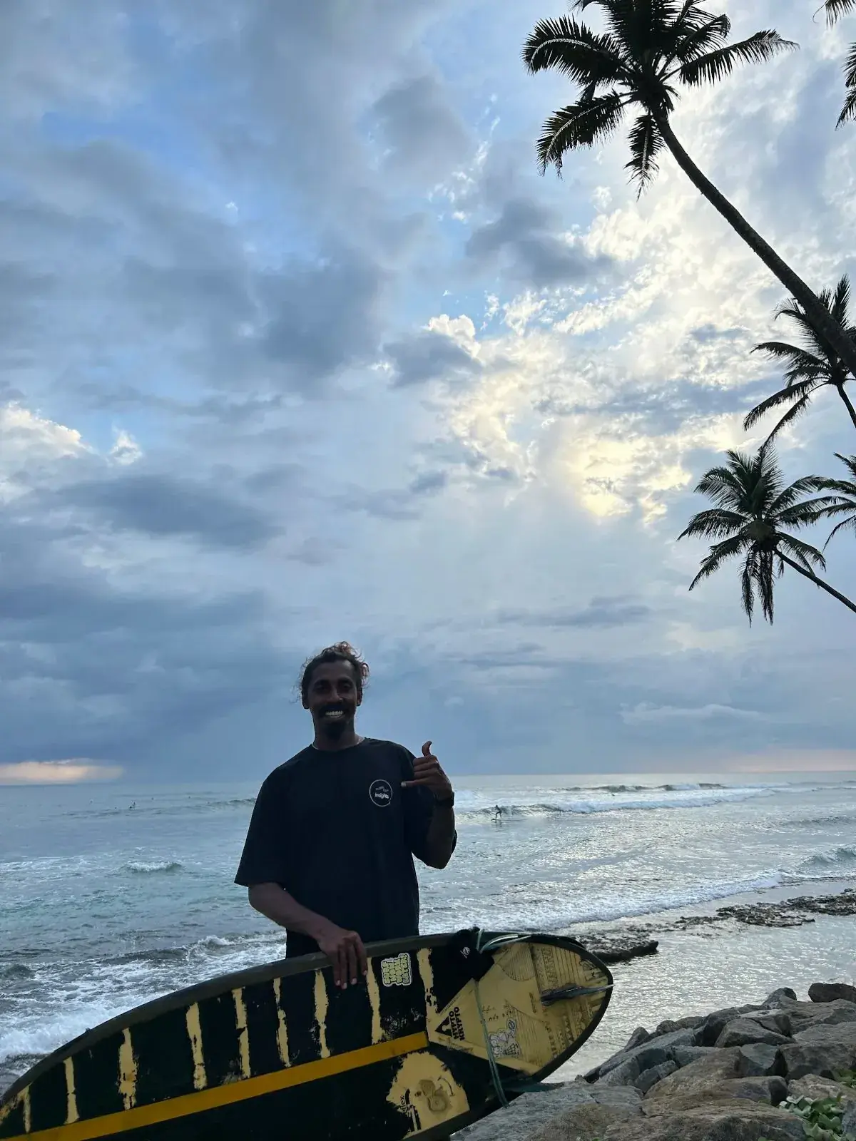 Instructor giving a shaka on the rocks with a board