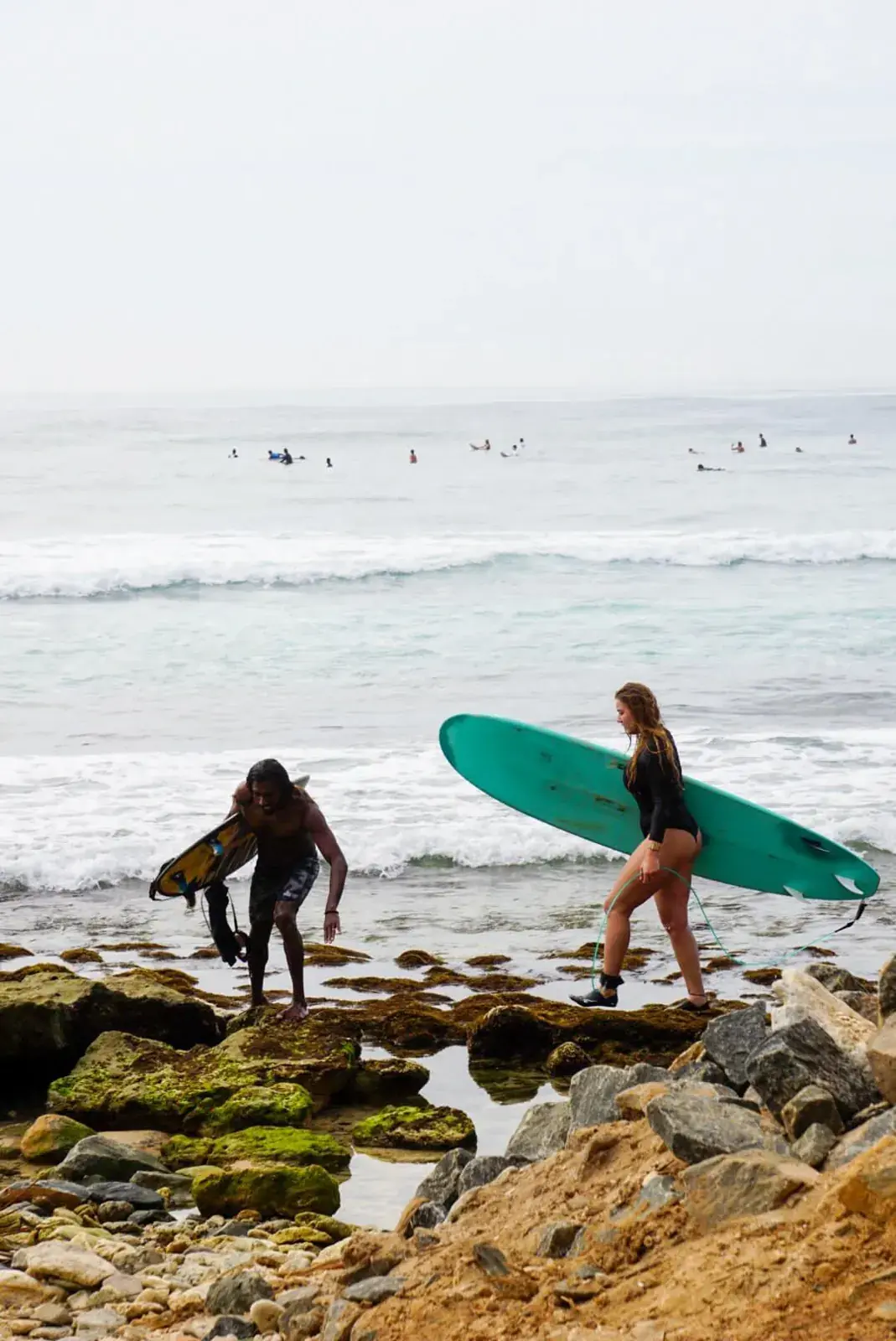 Two surfers stepping over rocks into the sea