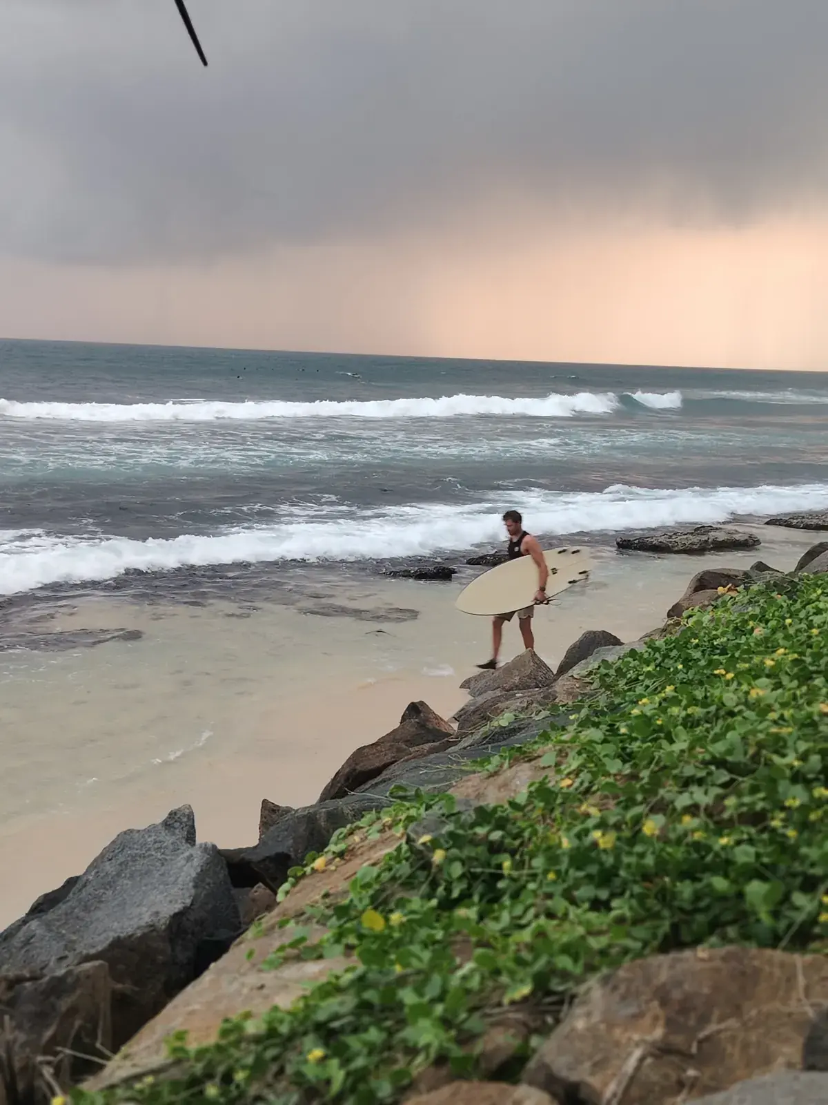Surfer walking along a rocky shore with a board as clouds roll in
