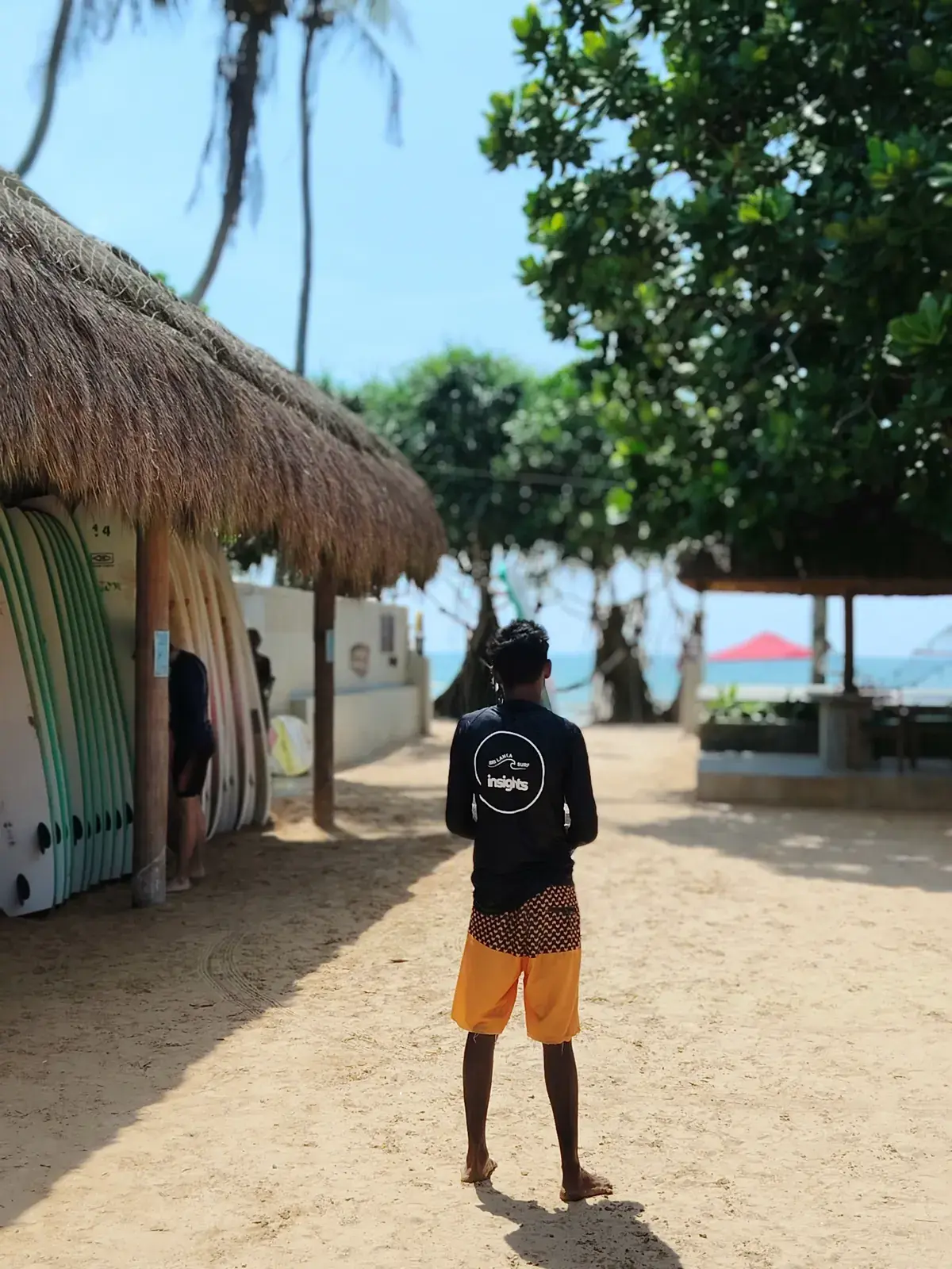Surfer walking past boards racked under a thatched roof