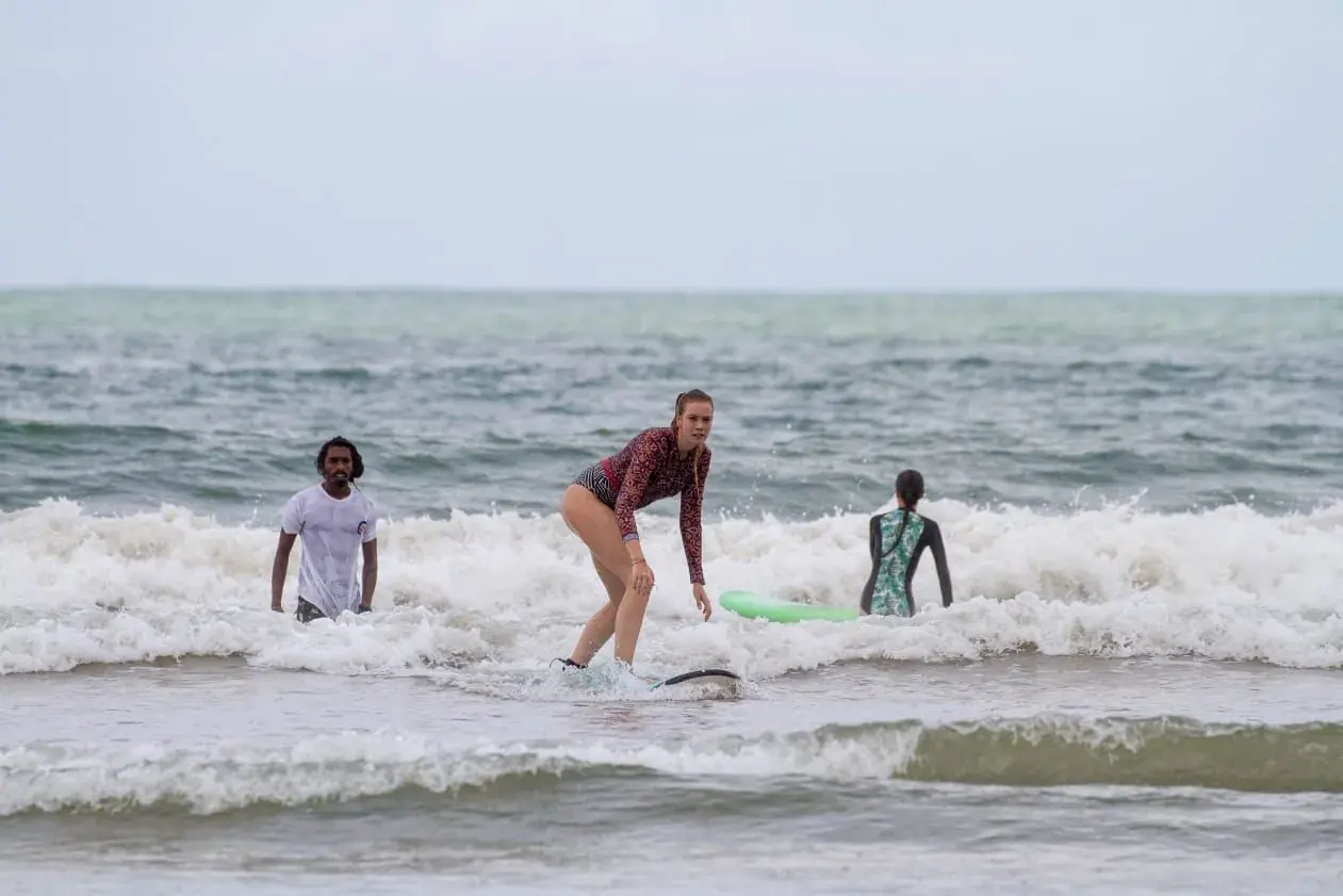 Student standing up on a board in the whitewater, instructors close by
