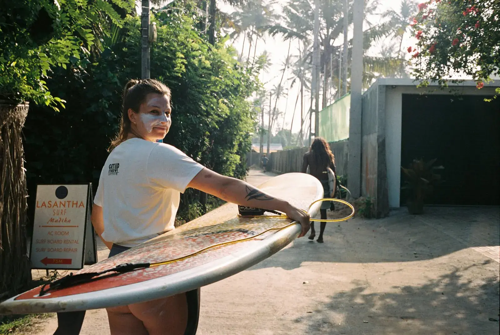 Guest carrying a surfboard along a sunny street