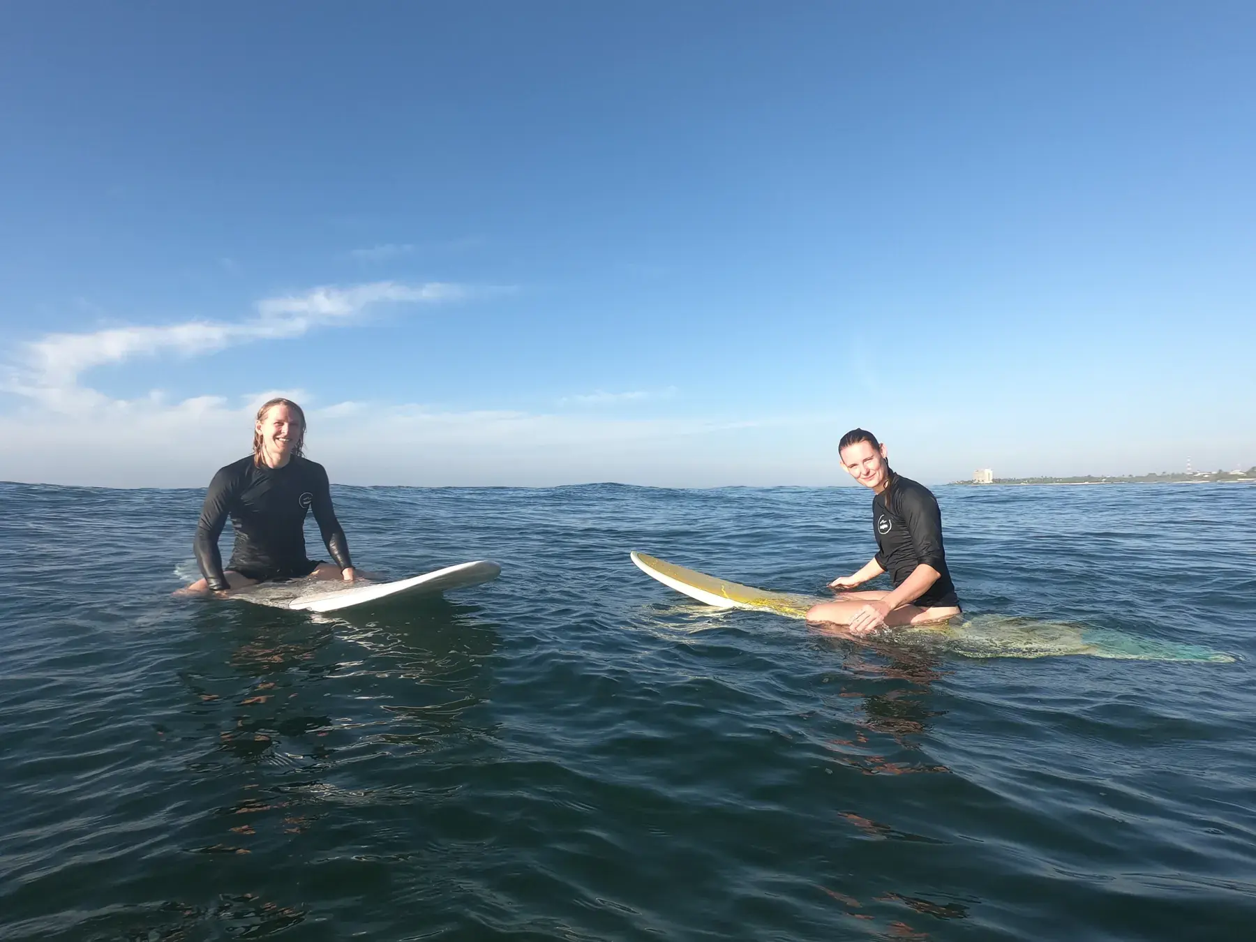 Two surfers sitting on their boards in the water, waiting for a wave