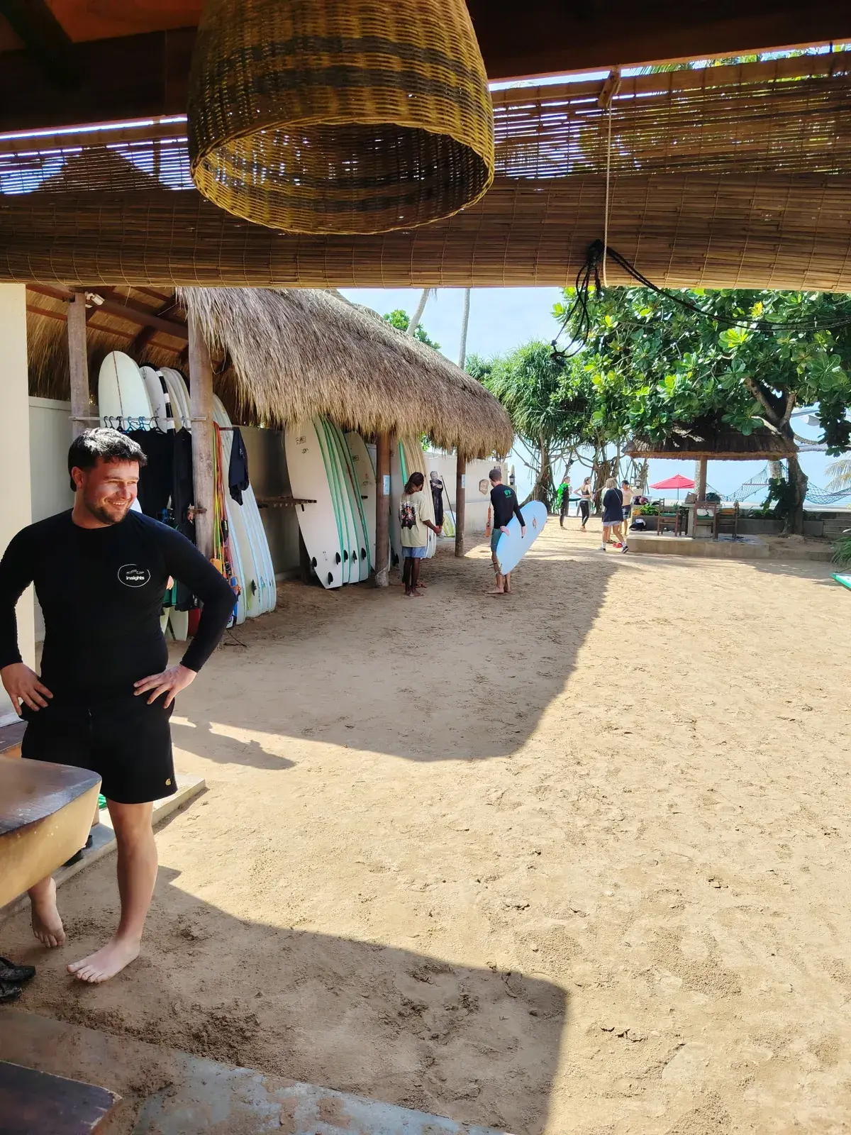 Surfer by a beach surf shop, boards racked under a thatched roof