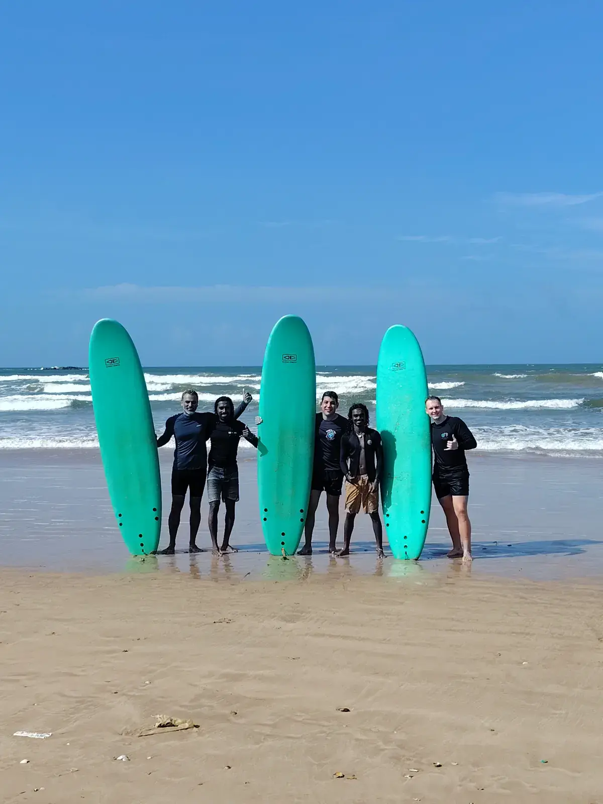 Group lined up on the beach with three teal boards