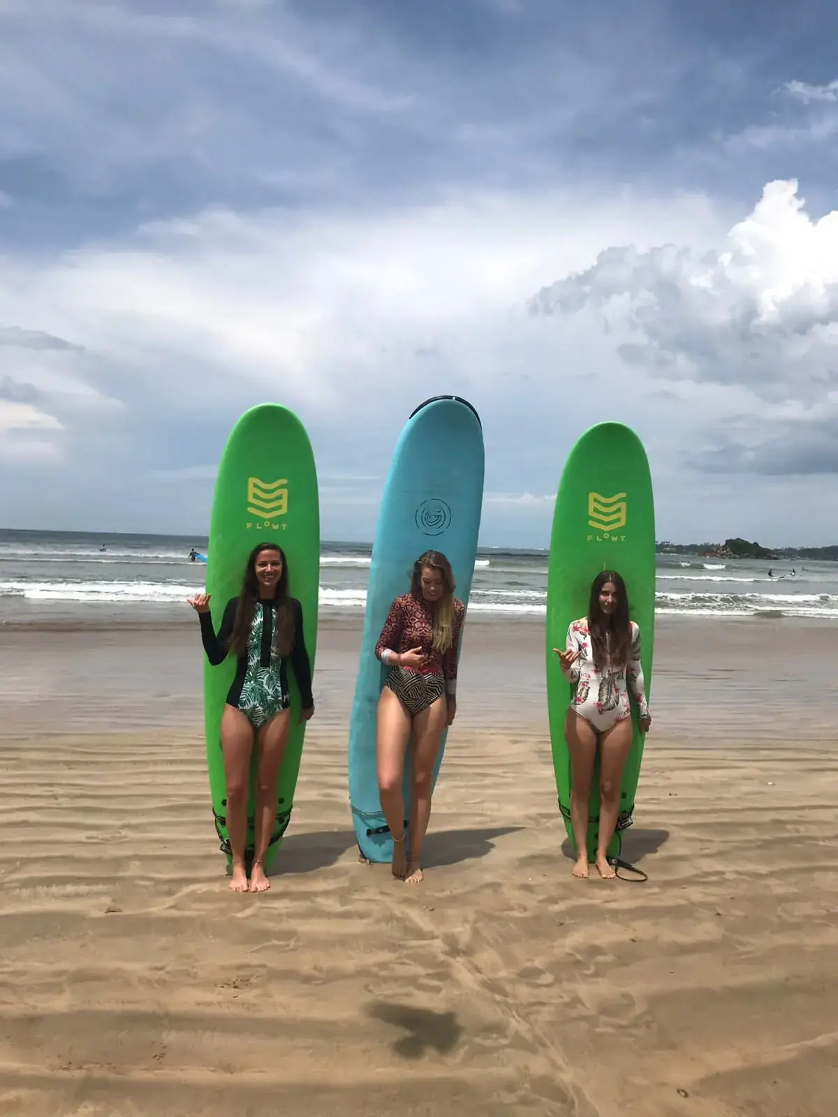 Three surfers standing behind tall boards on the beach