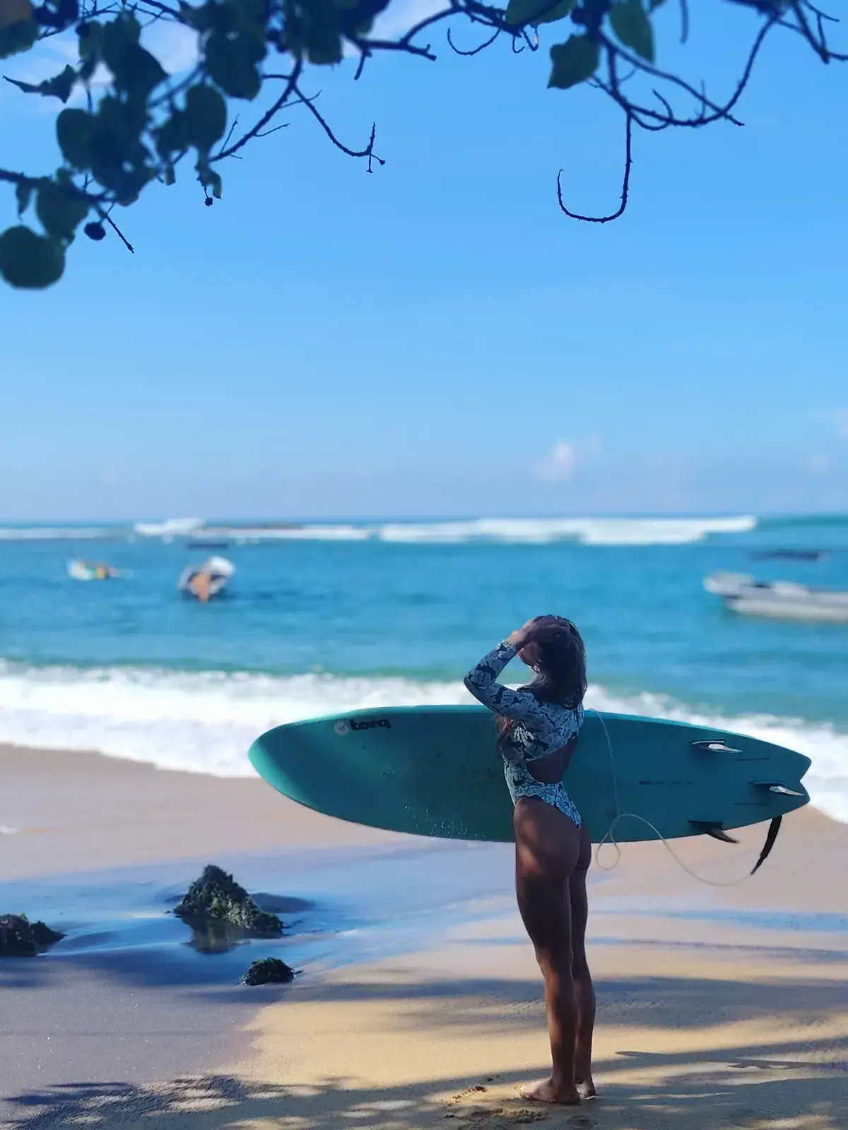 Surfer shading their eyes to watch the waves, board under one arm